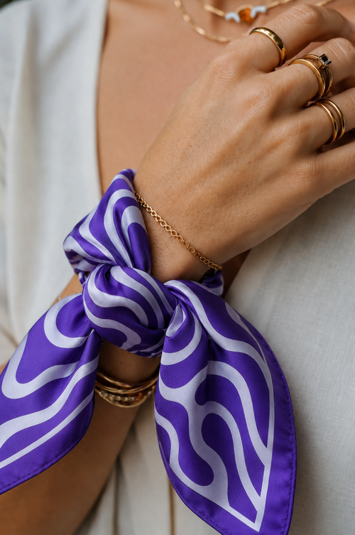 Close-up of a model styling the apashka Acid Wave purple silk scarf tied as a chic wrist accessory or bracelet, paired with gold rings and a white top.