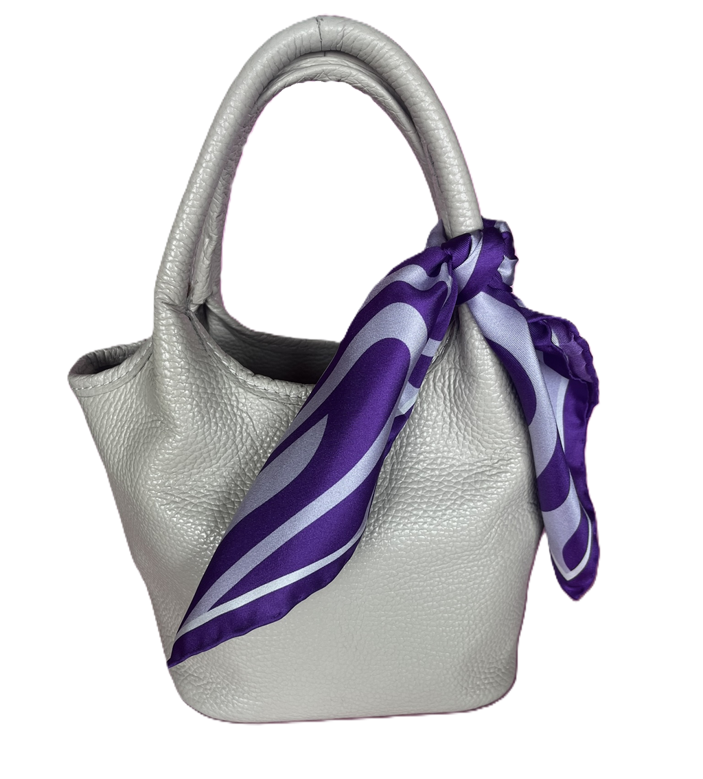 A white textured leather handbag with a apashka Acid Wave silk scarf tied around its handle.