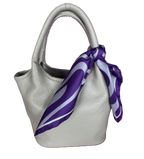 A white textured leather handbag with a apashka Acid Wave silk scarf tied around its handle.