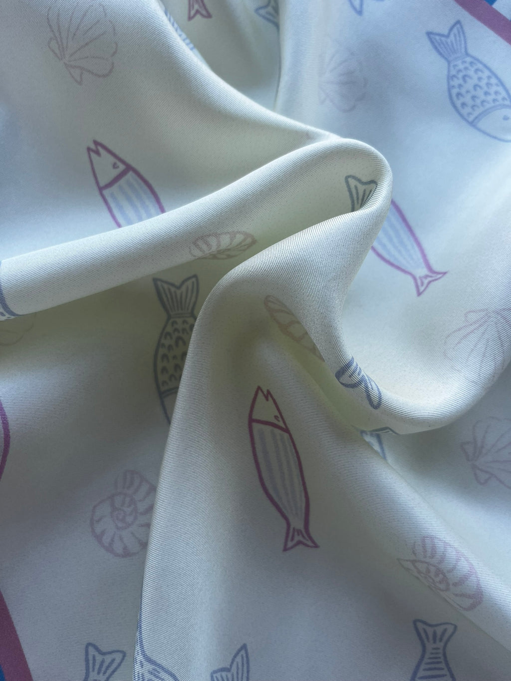 Close up of apashka Apashka Marina silk twill fabric folds showing the premium texture and pastel fish print detail.