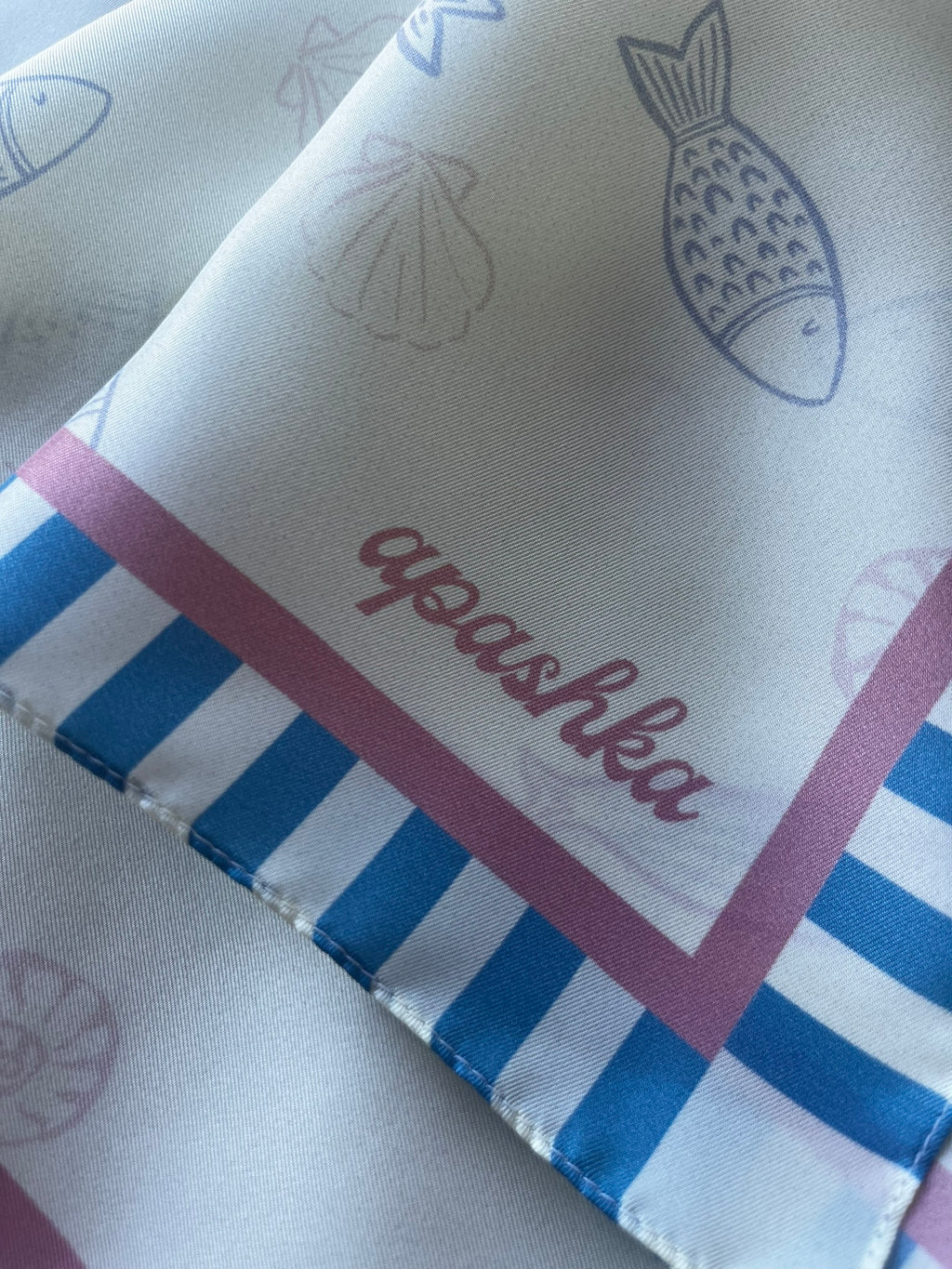 Close up of the signature apashka script logo on the Apashka Marina silk bandana corner with turquoise candy stripes.