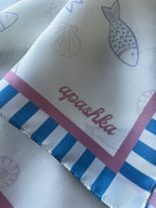 Close up of the signature apashka script logo on the Apashka Marina silk bandana corner with turquoise candy stripes.