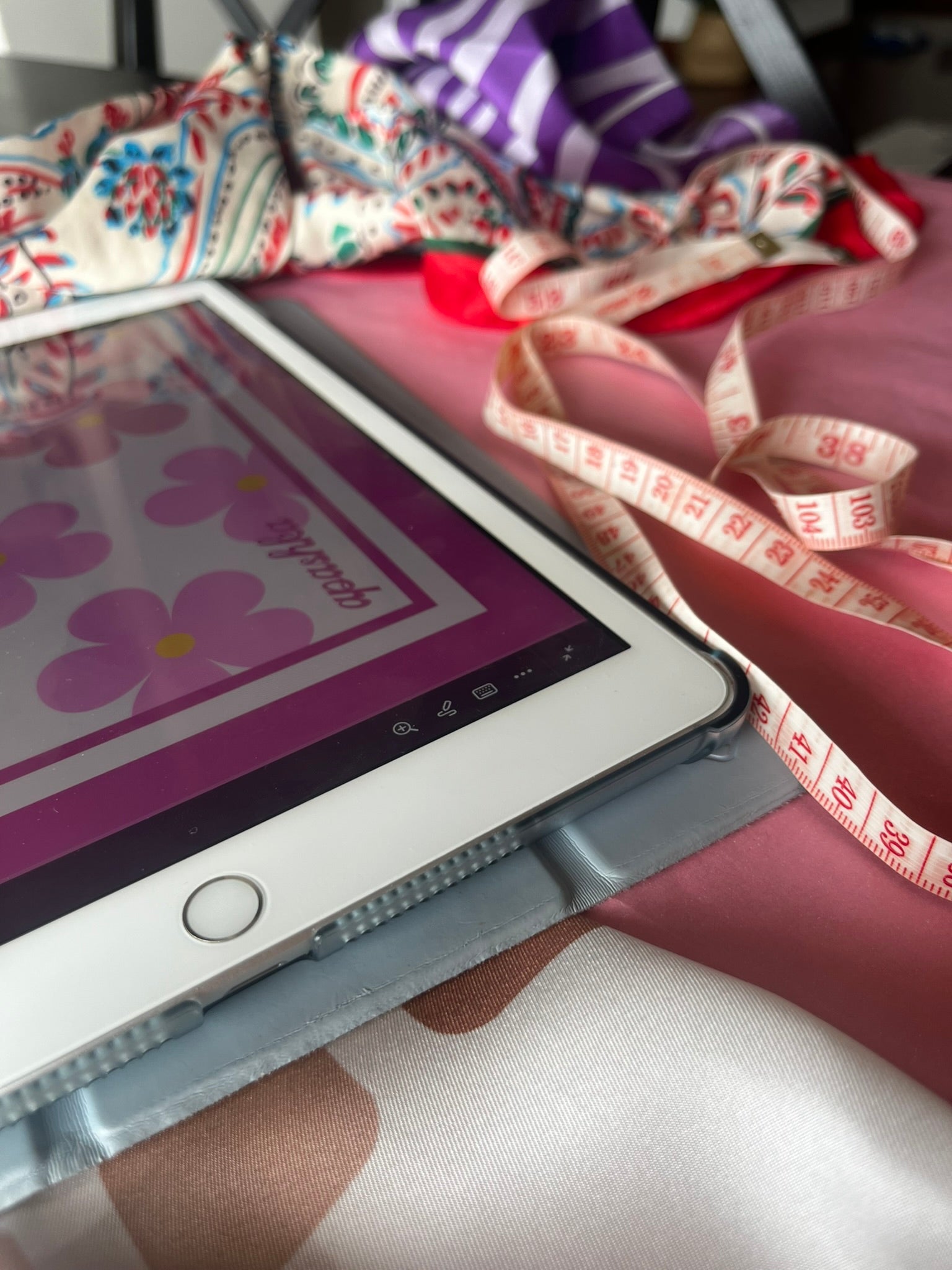 Tablet with a floral scarf pattern on screen, surrounded by colorful fabric and measuring tape.
