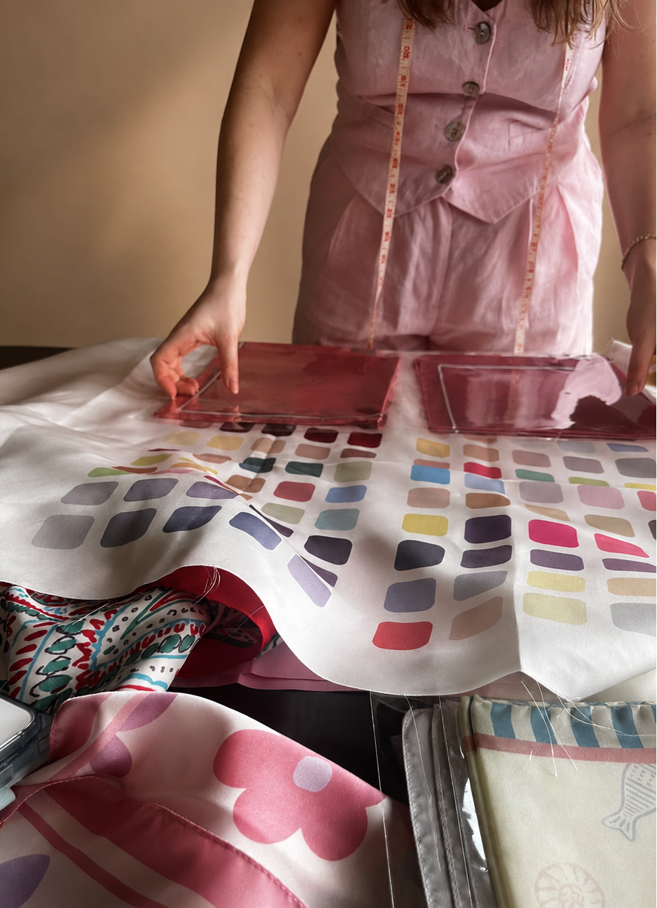 Person working with fabric swatches and a patterned fabric on a table.