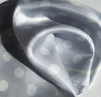 Close-up detail of the luxurious silk fabric texture of the apashka Bubble-Pop Blu silk scarf, highlighting the high-shine material, light blue color, and white polka dot print.