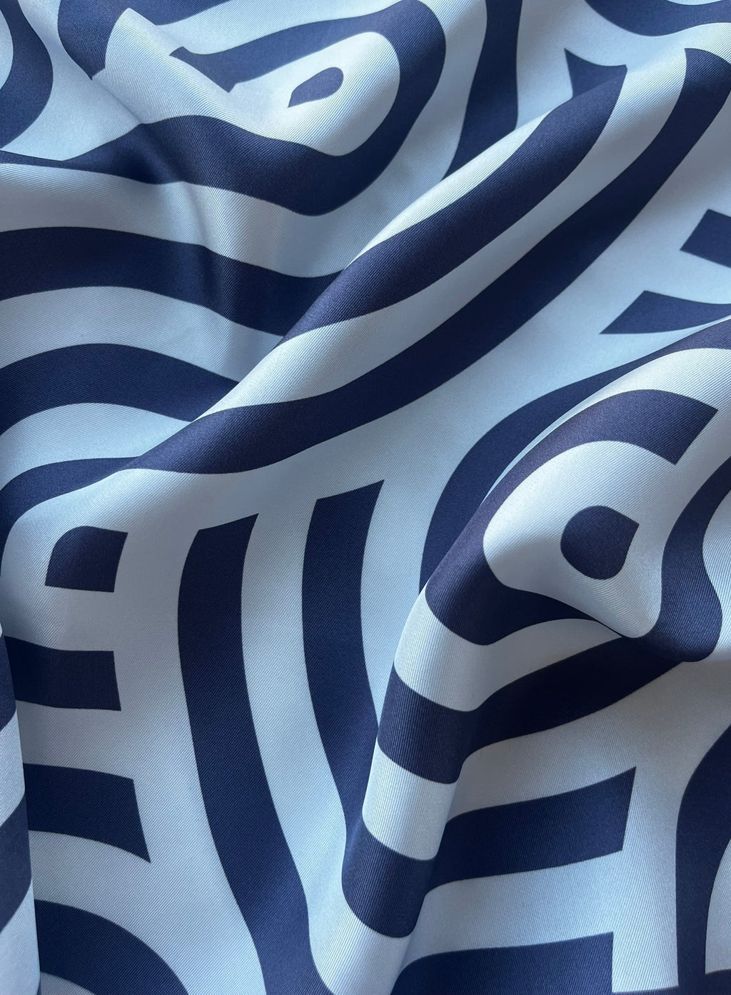 Close up of apashka Disco Waves silk twill fabric folds showing the premium texture and navy blue wavy print.