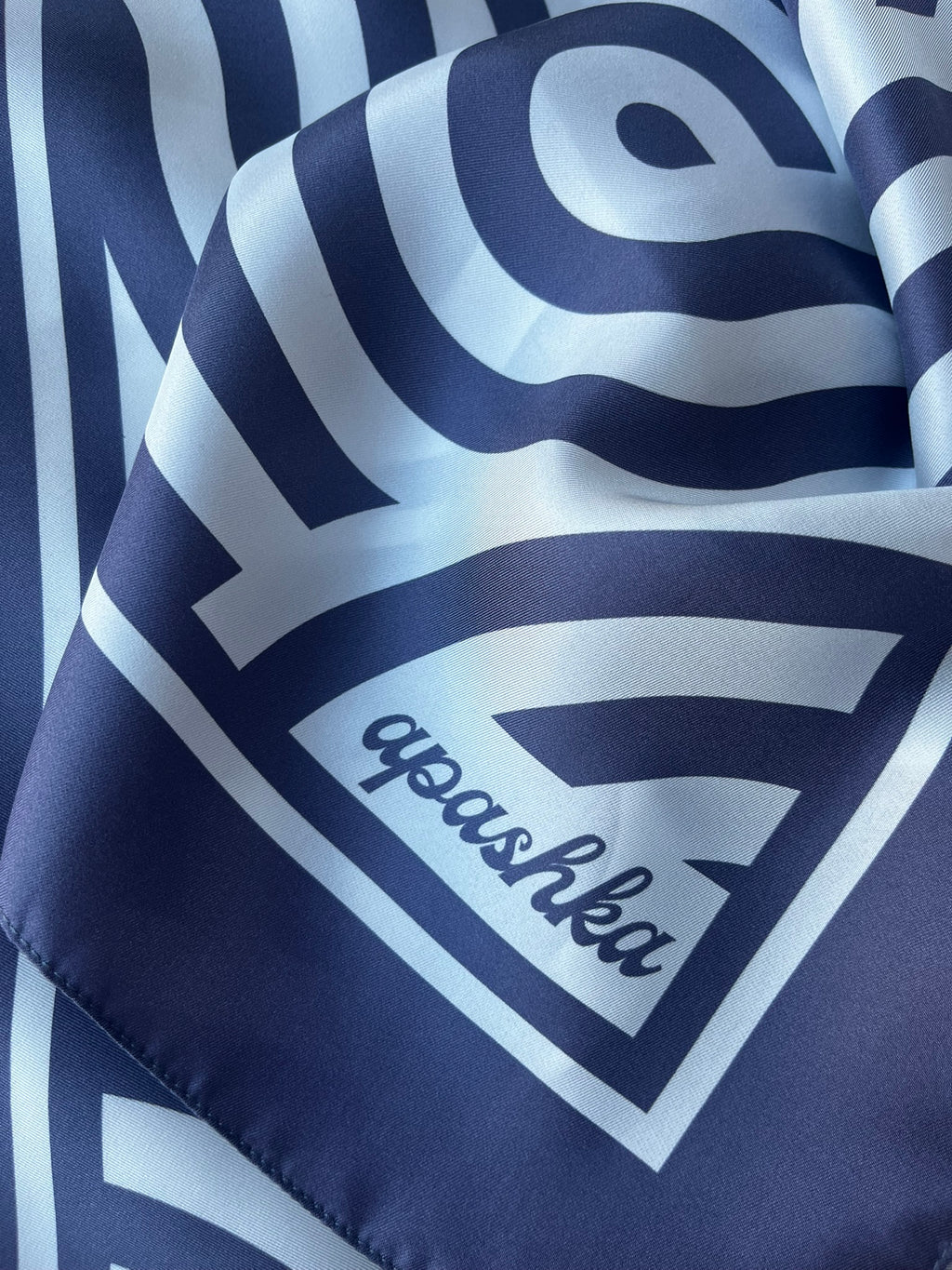 Close up of the signature apashka script logo printed on the corner frame of the navy blue silk foulard.