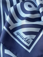 Close up of the signature apashka script logo printed on the corner frame of the navy blue silk foulard.
