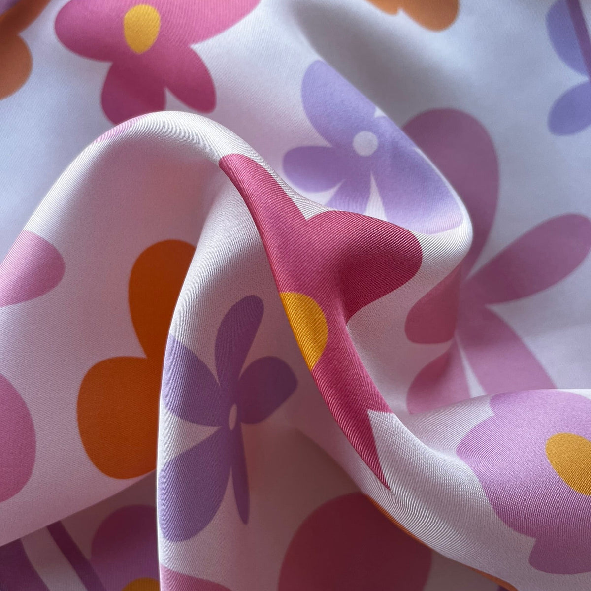 Close up of apashka Fiori Fuori silk twill fabric folds showing the retro pink, purple, and orange flower print texture.