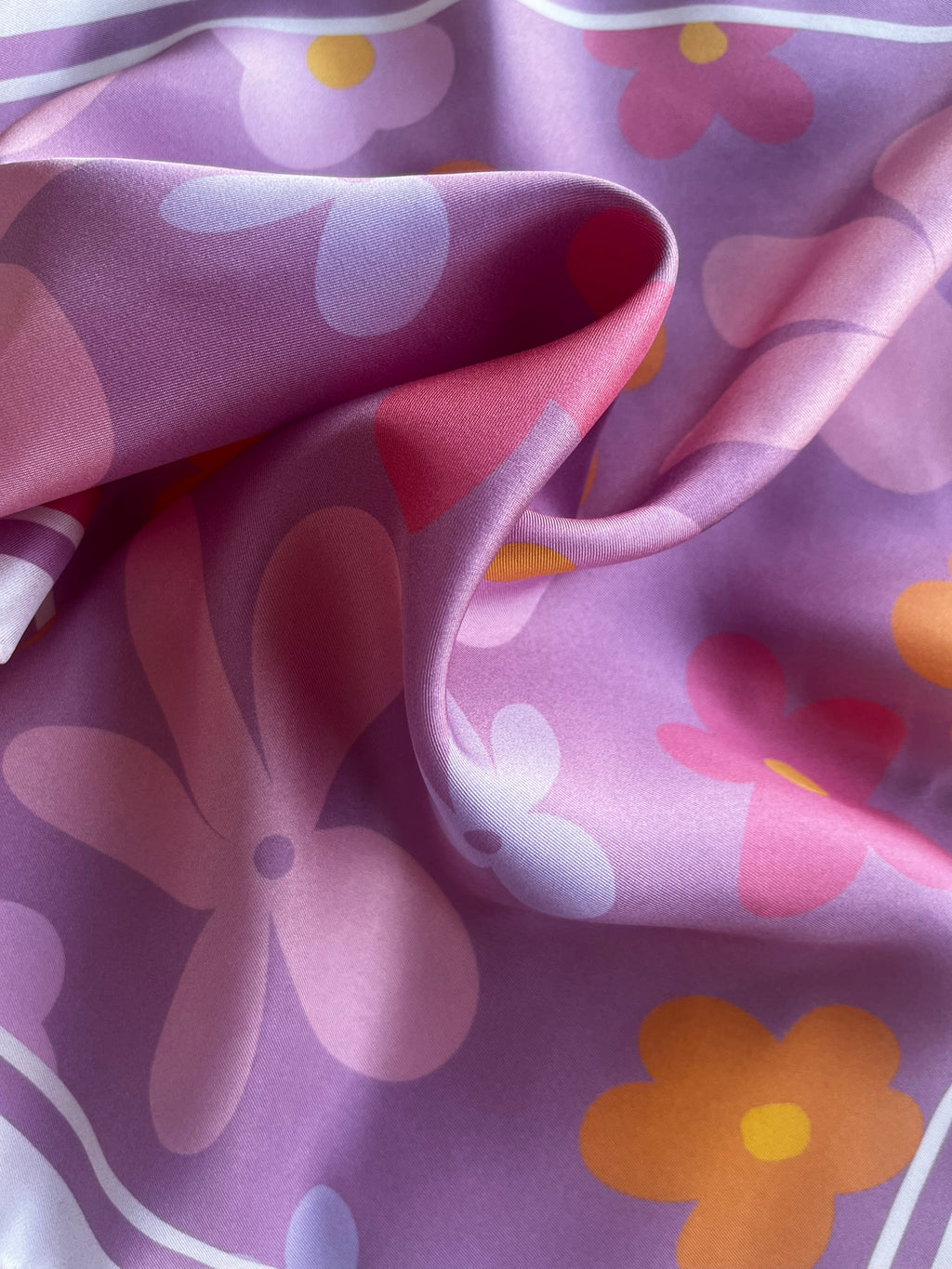 Close up of apashka Fiori Fuori silk twill fabric folds showing the retro pink, purple, and orange flower print texture.