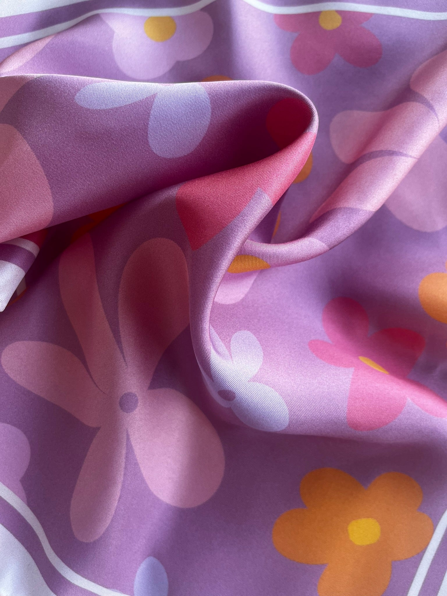 Close up of apashka Fiori Fuori silk twill fabric folds showing the retro pink, purple, and orange flower print texture.