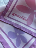 Close up of the signature apashka script logo on the lilac purple border corner of the retro floral silk bandana.