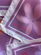 Close up of the signature apashka script logo on the lilac purple background and cream corner of the retro floral silk bandana.