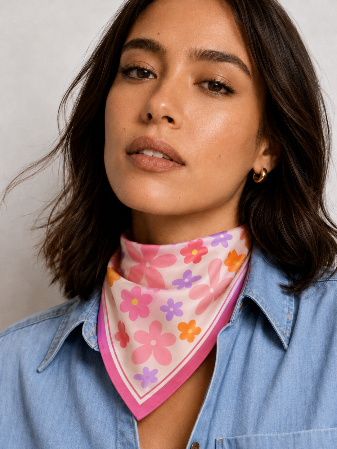 A model wearing the apashka Fiori Fuori pink floral silk bandana tied as a front-knot neckerchief, styled with a casual blue denim shirt.
