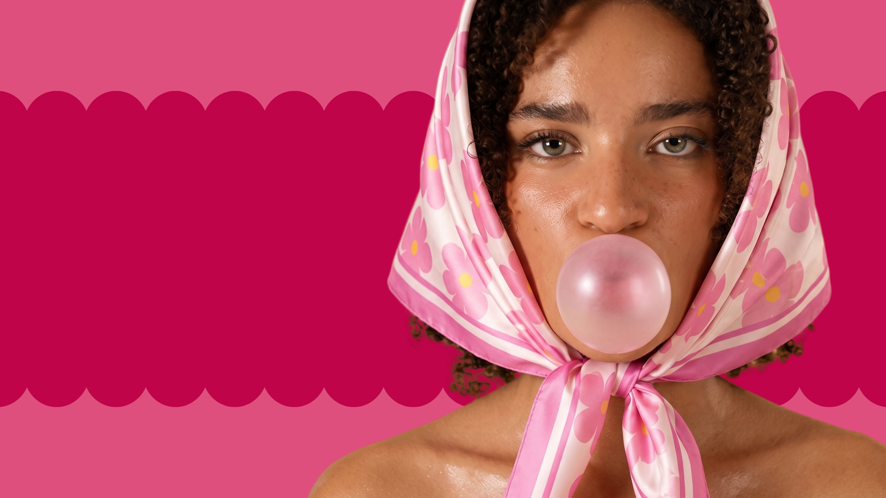 A close-up portrait of a woman with curly dark hair wearing a pink and white patterned silk headscarf tied under her chin, blowing a pink bubblegum bubble. The background is a vibrant pink with a scalloped magenta border.