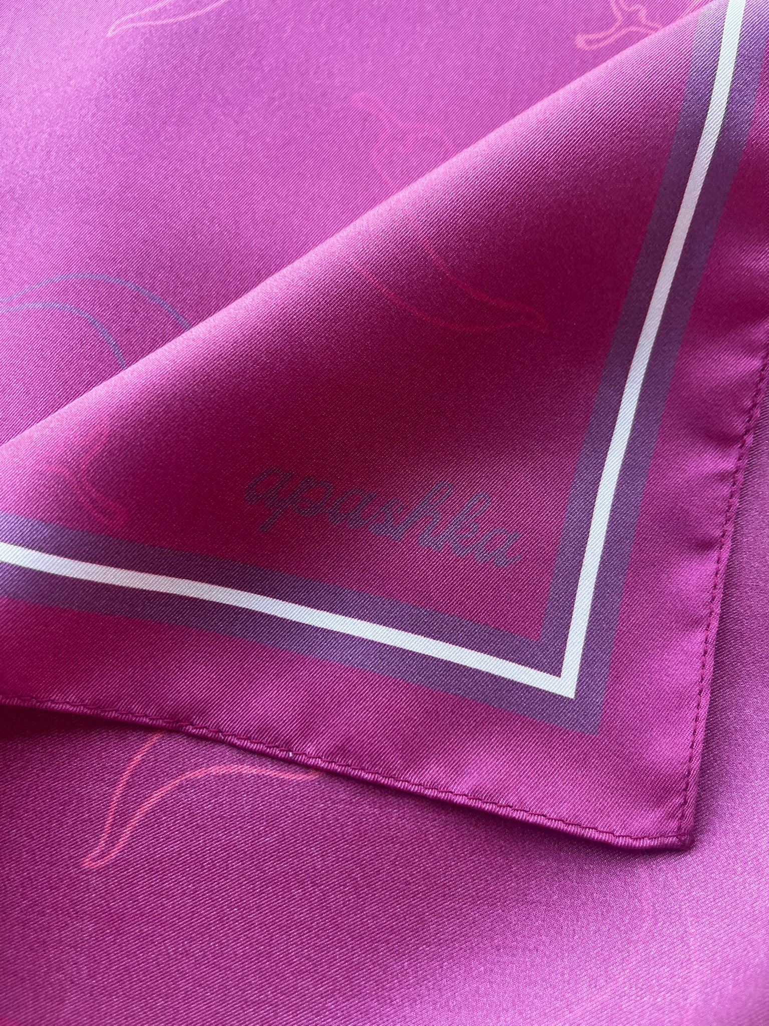 Close up of the signature apashka script logo on the corner of the silk bandana in dark magenta colour.