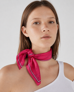 Model wearing the apashka Red Hot Chili Apashka crimson silk bandana, tied as a front-knot neckerchief to showcase the chili pattern and border, paired with a white tank top.
